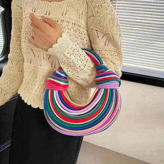 Woman holding a colorful striped handbag while wearing a cream sweater and black skirt.
